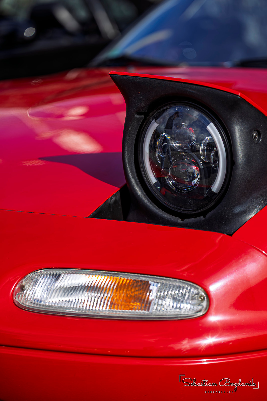 Two Miatas: a real one with pop-up headlights, and a toy one with sleepy eyelids and its tongue out (1/2)
