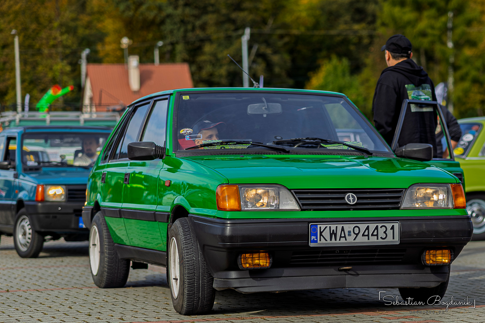 Zielony Polonez Caro wjeżdża na plac, za nim inne klasyczne auta.
