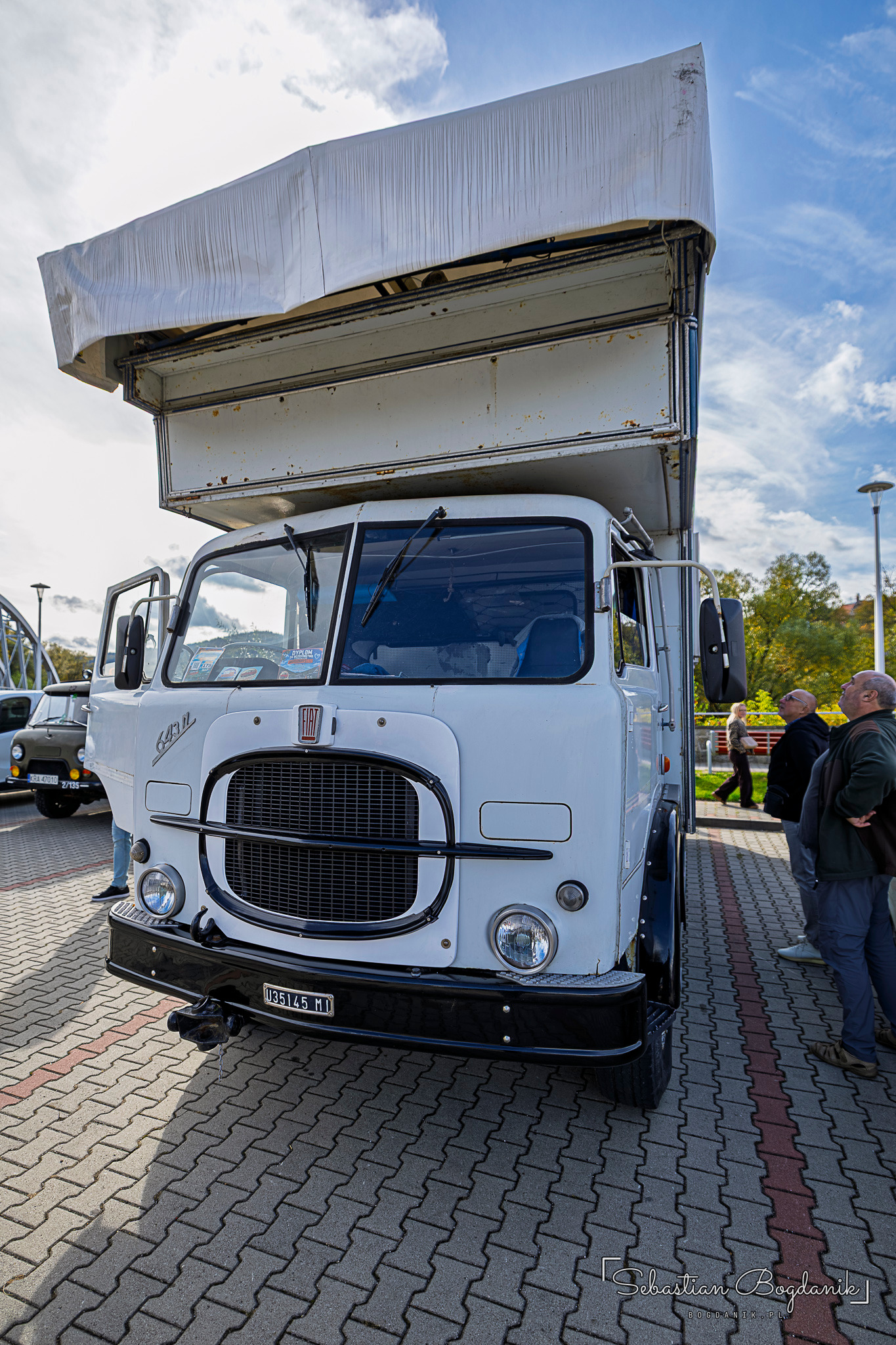 Biała ciężarówka Fiat z dużym grillem i drewniano-białą zabudową mieszkalną na podwoziu.